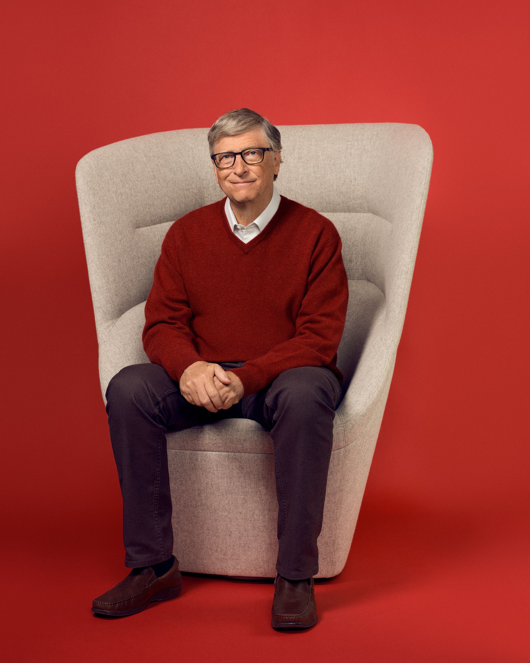 Still image of Bill Gates in front of a red background, sitting